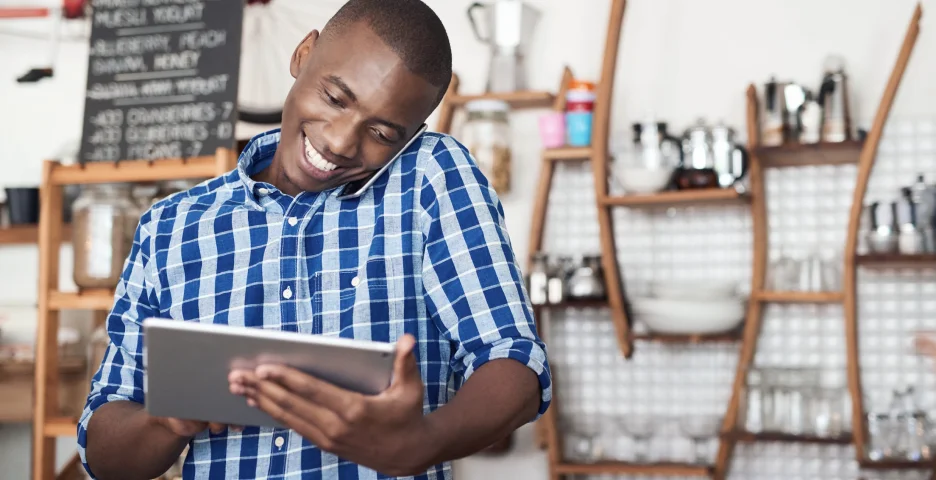 Smiling small business owner multitasking with a tablet and phone in a modern café.
