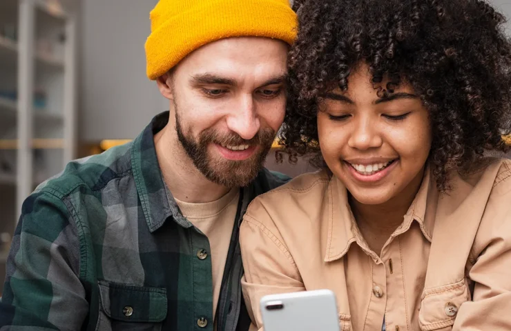 Happy couple sitting beside each other looking at their smartphone at digital banking services