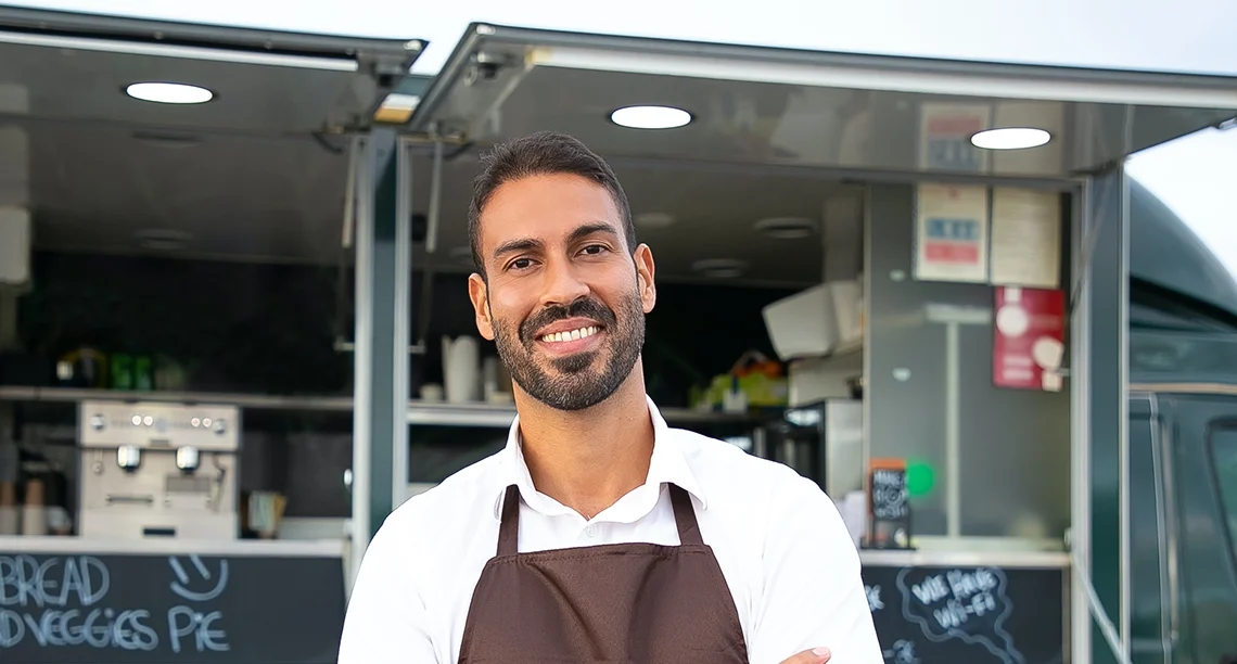 Small business owner smiling in front of his food truck.