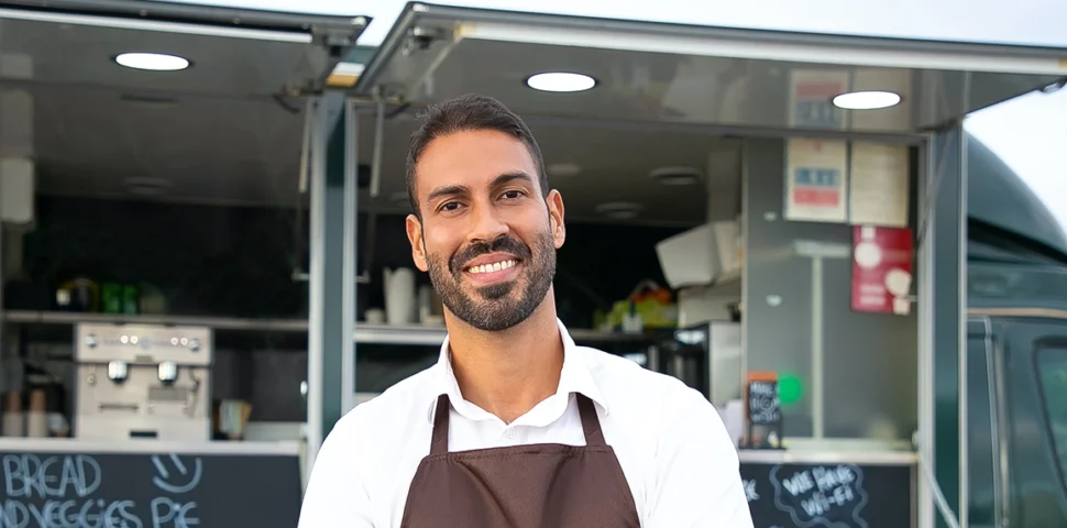 Small business owner smiling in front of his food truck.