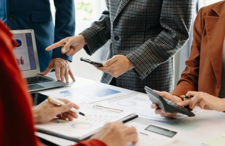 Close-up of business professionals using mobile devices and reviewing documents during a meeting.