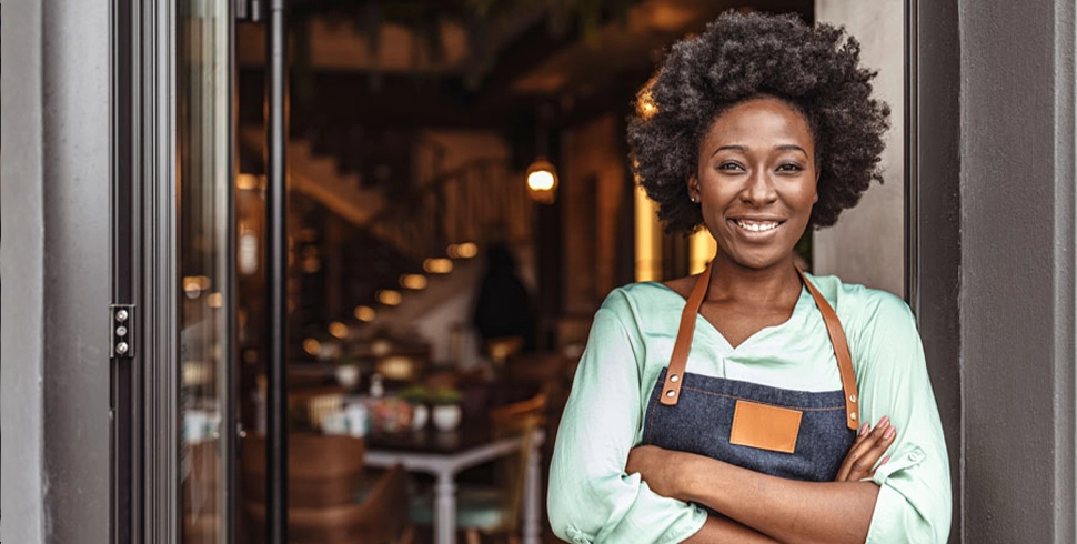 Confident female business owner standing with arms crossed at shop entrance