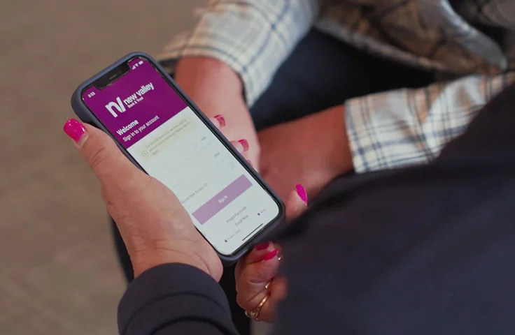 Customer using the New Valley Bank mobile app on a smartphone during a banking appointment.