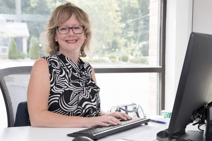 Smiling New Valley Bank employee working at a computer desk in a bright office environment.